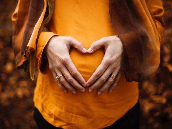 Pregnant woman putting her hands on her stomach to make a heart shape