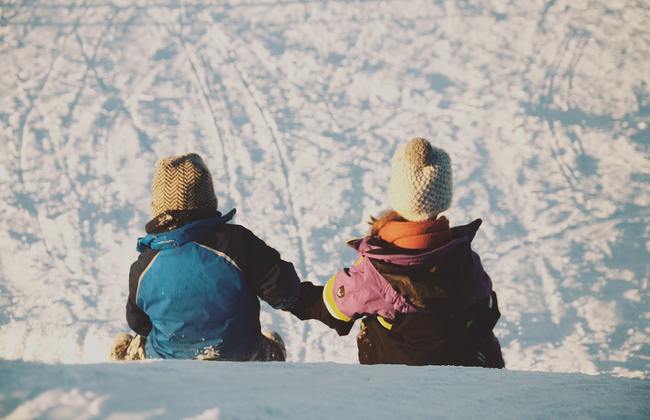 Two children holding hands as they sledge down a snowy hill