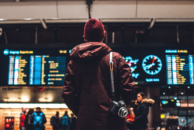 Man wearing jacket and wooly hat looks at departure boards in an airport